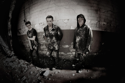 a black-and-white photo of three of shadowplay bands members standing in front of a brick wall