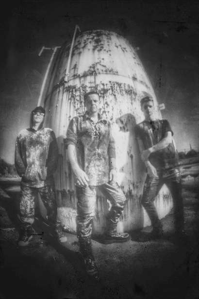 a black and white photo of three shadowplay band mates  the rock industrial group from Asheville nc standing in front of an old building